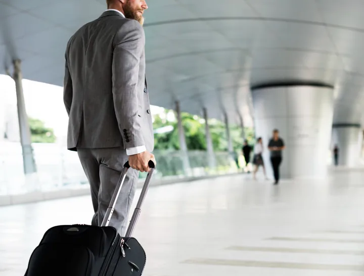Executivo caminhando com mala de rodinhas no aeroporto